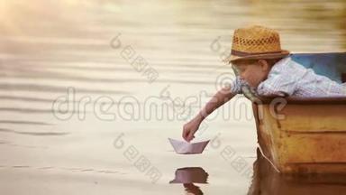 划片镜头：小男孩坐在真正的船上，让他的纸船启航